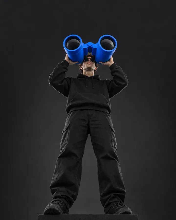 Person sucht mit einem übergroßen blauen Fernglas den Horizont ab